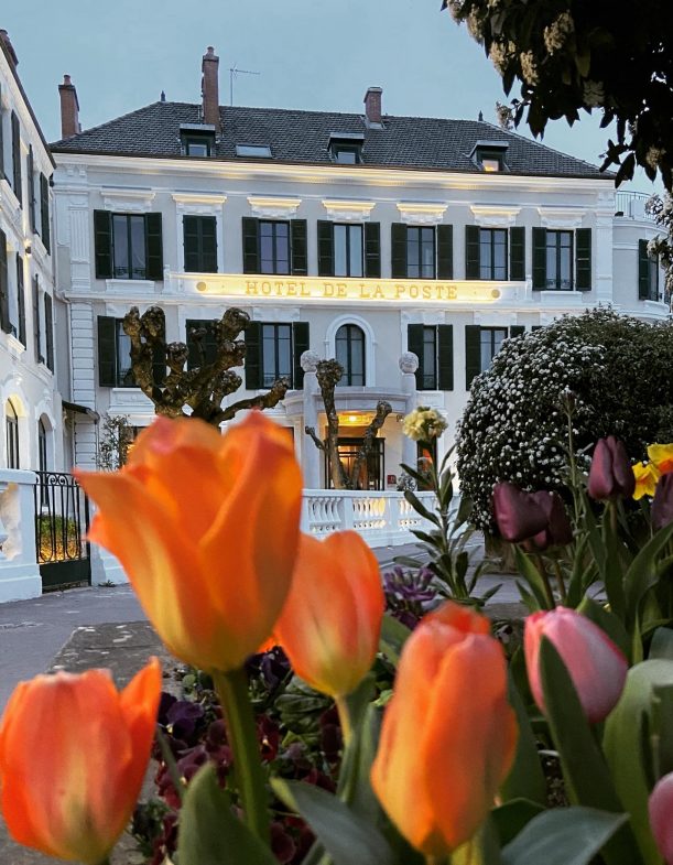 The pretty façade of the Hôtel de la Poste in Beaune, Burgundy, with orange tulips in the foreground, in the evening